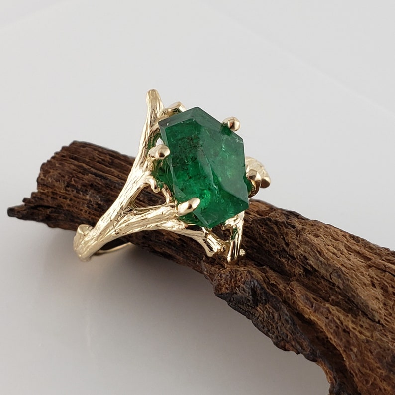 Puede incluir: Un anillo de oro con una gran esmeralda facetada engastada en un dise&ntilde;o de rama.
