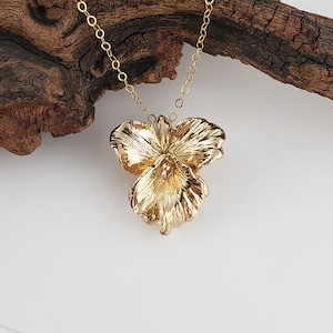 May include: A gold-toned necklace with a delicate chain and a pendant shaped like a three-petal flower.