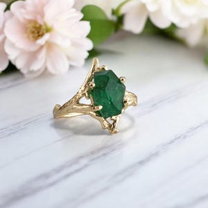 Puede incluir: Un anillo de oro con una piedra preciosa verde engastada en un dise&ntilde;o de ramas.