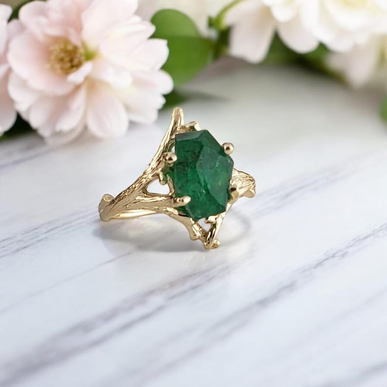 Puede incluir: Un anillo de oro con una piedra preciosa verde engastada en un dise&ntilde;o de ramas.