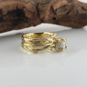 May include: A gold ring with a rough, grey diamond set in a branch-like band. The ring is designed to look like a piece of nature.