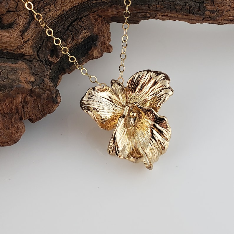 May include: A gold necklace with a delicate flower pendant. The flower is made of textured metal and has a three-dimensional design.
