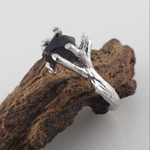 May include: A silver ring with a dark red gemstone set in a branch-like design.