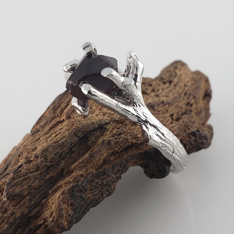 May include: A silver ring with a dark red gemstone set in a branch-like design.