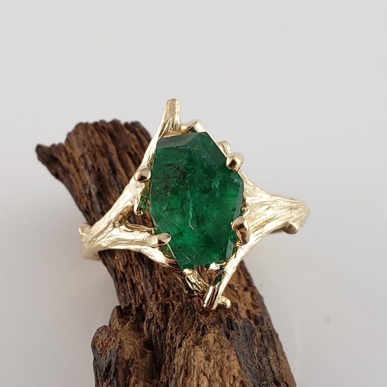 Puede incluir: Un anillo de oro con una gran esmeralda facetada engastada en un dise&ntilde;o de rama.