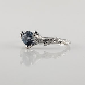 May include: A silver ring featuring a blue gemstone set in a branch-like band.