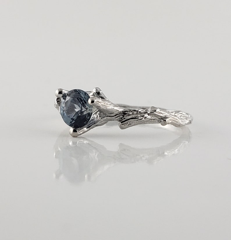 May include: A silver ring featuring a blue gemstone set in a branch-like band.