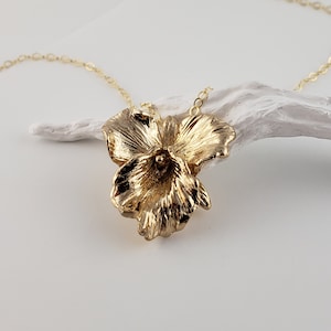 May include: A gold necklace with a three-dimensional flower pendant. The flower is made of textured metal and has a delicate, feminine design.