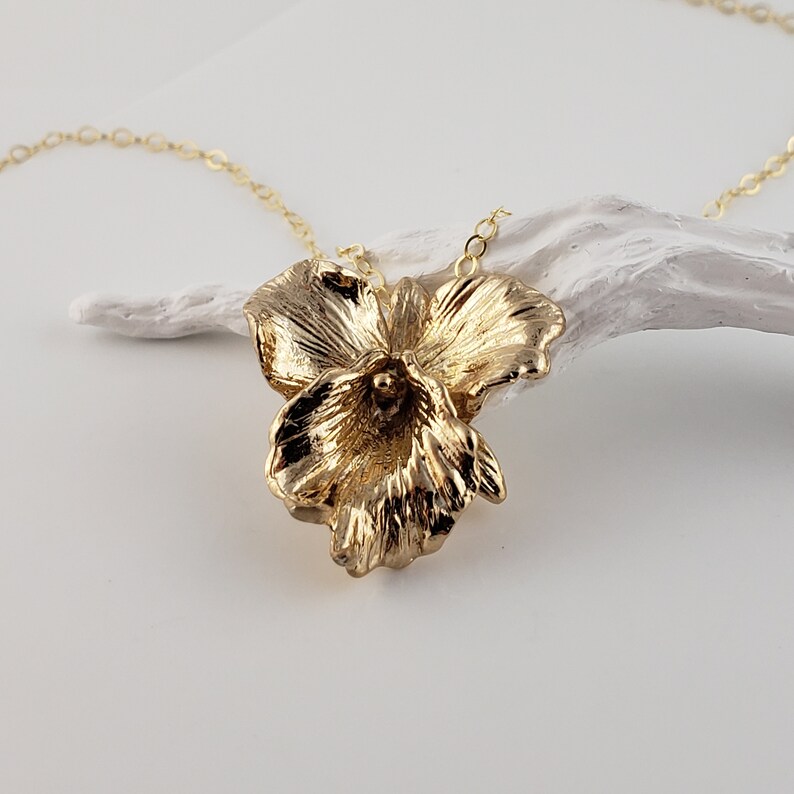 May include: A gold necklace with a three-dimensional flower pendant. The flower is made of textured metal and has a delicate, feminine design.