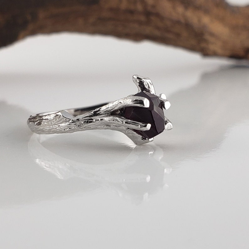 May include: A silver ring with a dark purple gemstone set in a branch-like design.