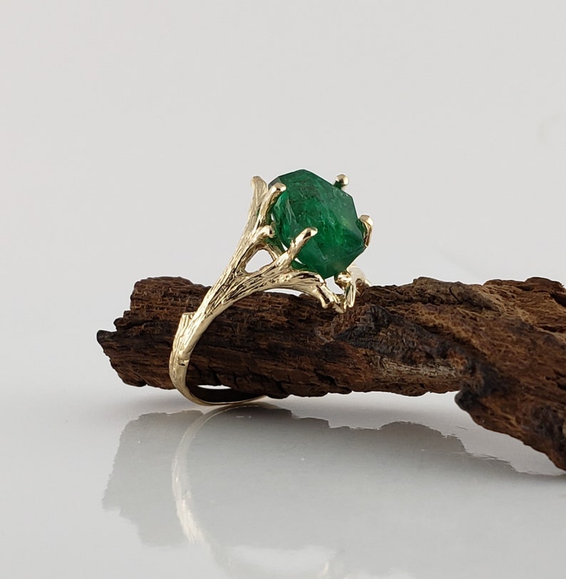 Puede incluir: Un anillo de oro con una gran esmeralda facetada engastada en un dise&ntilde;o de rama.