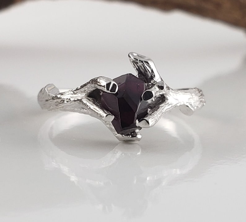 May include: A silver ring with a dark purple gemstone set in a branch-like design.