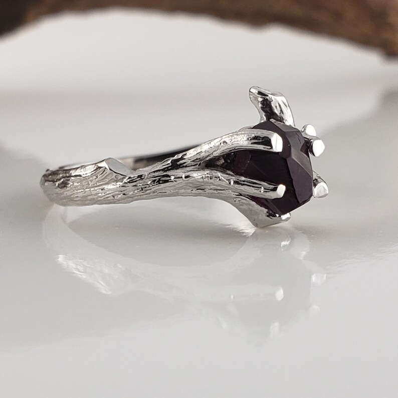 May include: A silver ring with a dark purple gemstone set in a branch-like design.