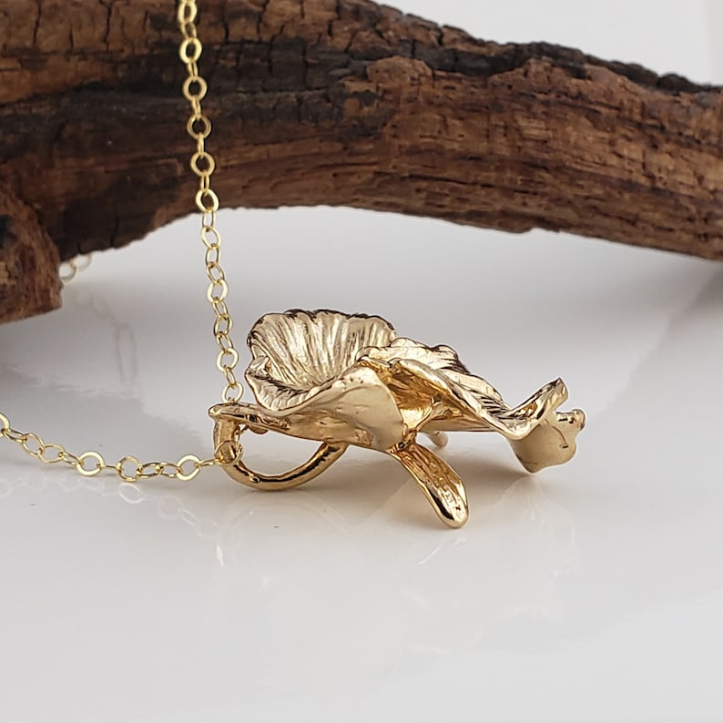 May include: A gold chain necklace with a pendant shaped like an orchid flower.