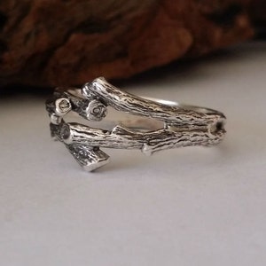 May include: A silver ring featuring a design of interwoven branches. The branches are textured to resemble real wood.
