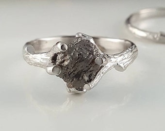 May include: A silver ring with a rough, gray gemstone set in a branch-like band.