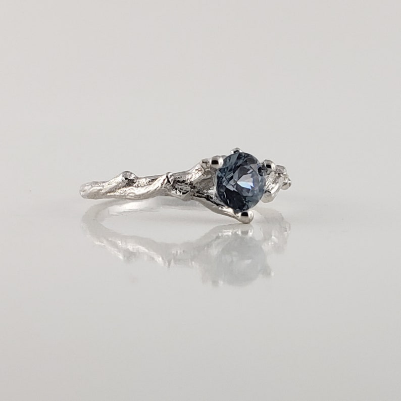 May include: A silver ring featuring a blue gemstone set in a branch-like design.