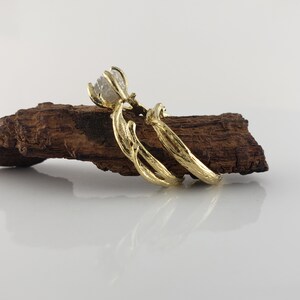 May include: A pair of gold rings with a rough diamond set in the center of the top ring. The rings are designed to look like intertwined branches.