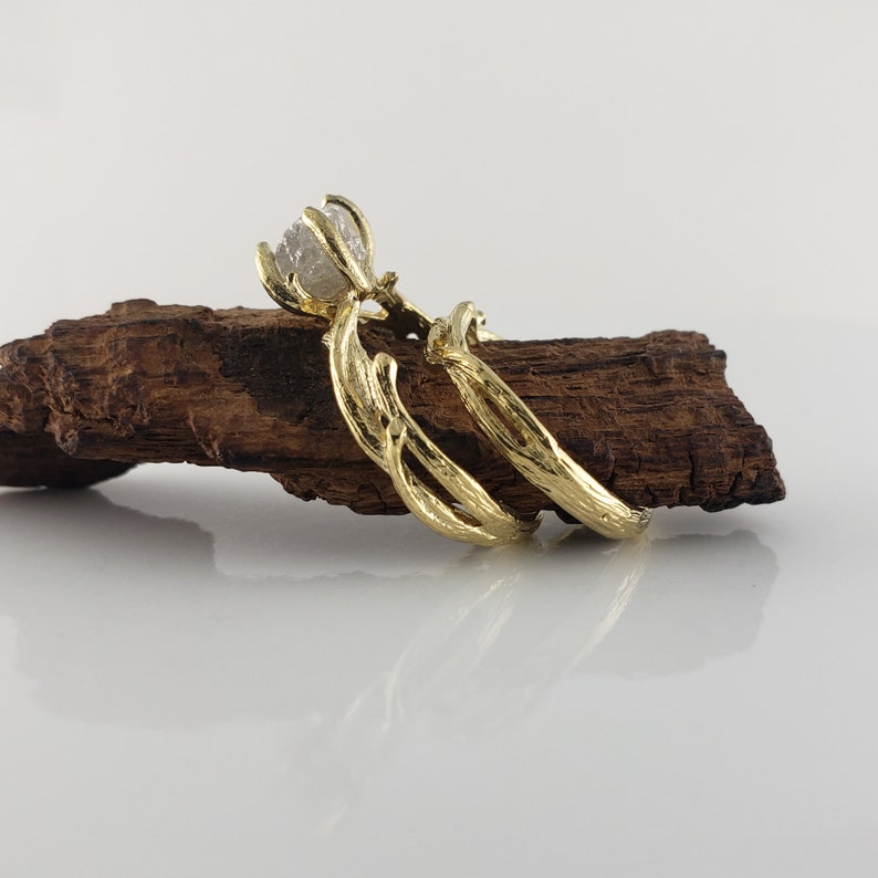 May include: A pair of gold rings with a rough diamond set in the center of the top ring. The rings are designed to look like intertwined branches.