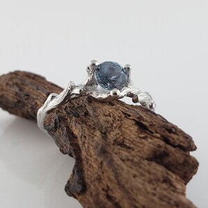 May include: A silver ring featuring a blue gemstone set in a branch-like design.