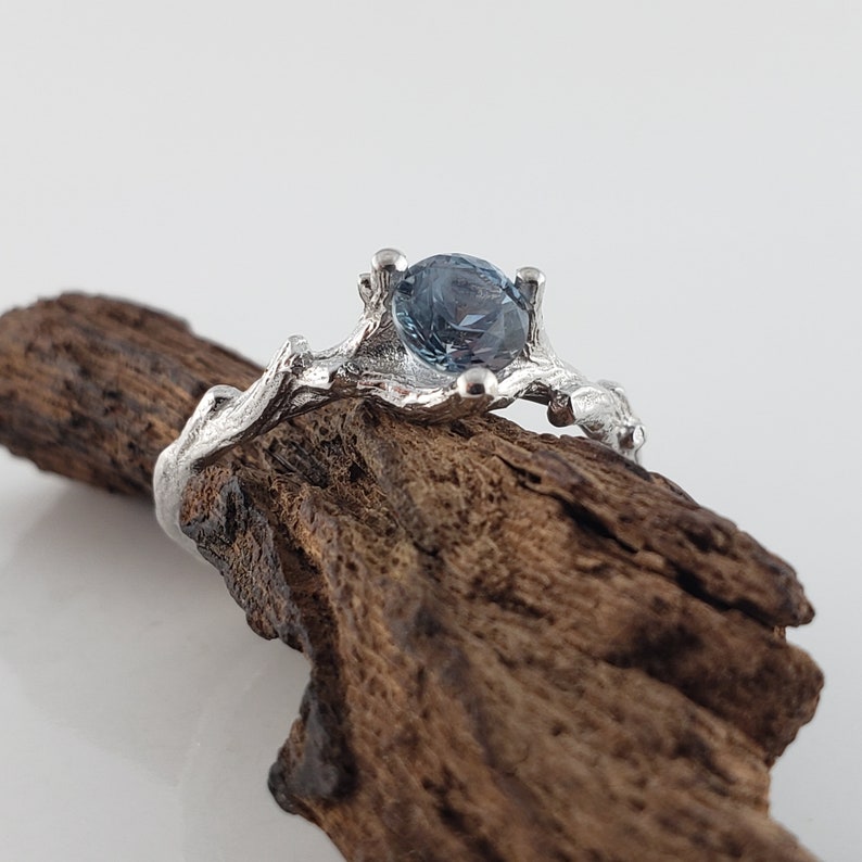 May include: A silver ring featuring a blue gemstone set in a branch-like design.