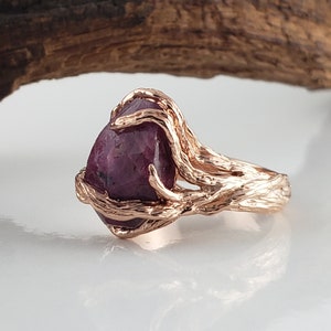 Könnte beinhalten: Ein Ring aus Roségold mit einem großen, facettierten Rubin, der in einem gedrehten Astdesign gefasst ist.
