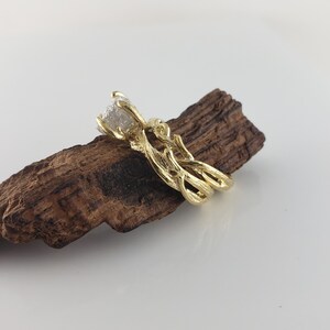 May include: A gold ring with a rough diamond set in a branch-like design. The ring is displayed on a piece of driftwood.