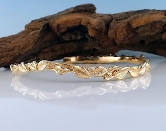 May include: A gold bangle bracelet with a delicate leaf design. The bracelet is made of a smooth, shiny metal and features a repeating pattern of leaves.