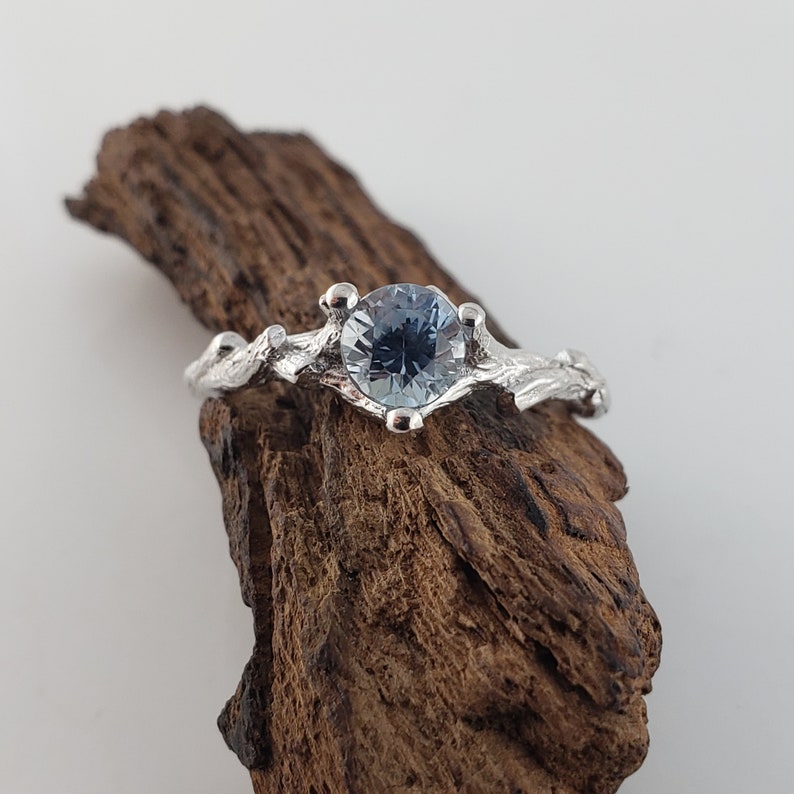 May include: A silver ring featuring a blue gemstone set in a branch-like design.