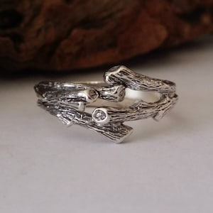 May include: A silver ring featuring a design of intertwined branches. The ring has a rustic, natural look and features small clear stones.