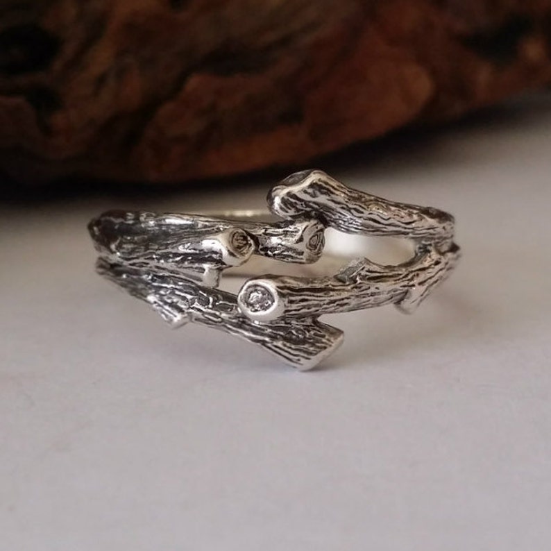 May include: A silver ring featuring a design of intertwined branches. The ring has a rustic, natural look and features small clear stones.