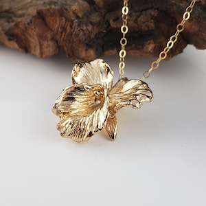 May include: A gold orchid pendant necklace with a detailed, textured design. The pendant is attached to a delicate gold chain.