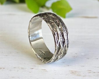 Puede incluir: Un anillo de plata con un diseño texturizado que se asemeja a la corteza de un árbol. El anillo es ancho y tiene un acabado pulido.