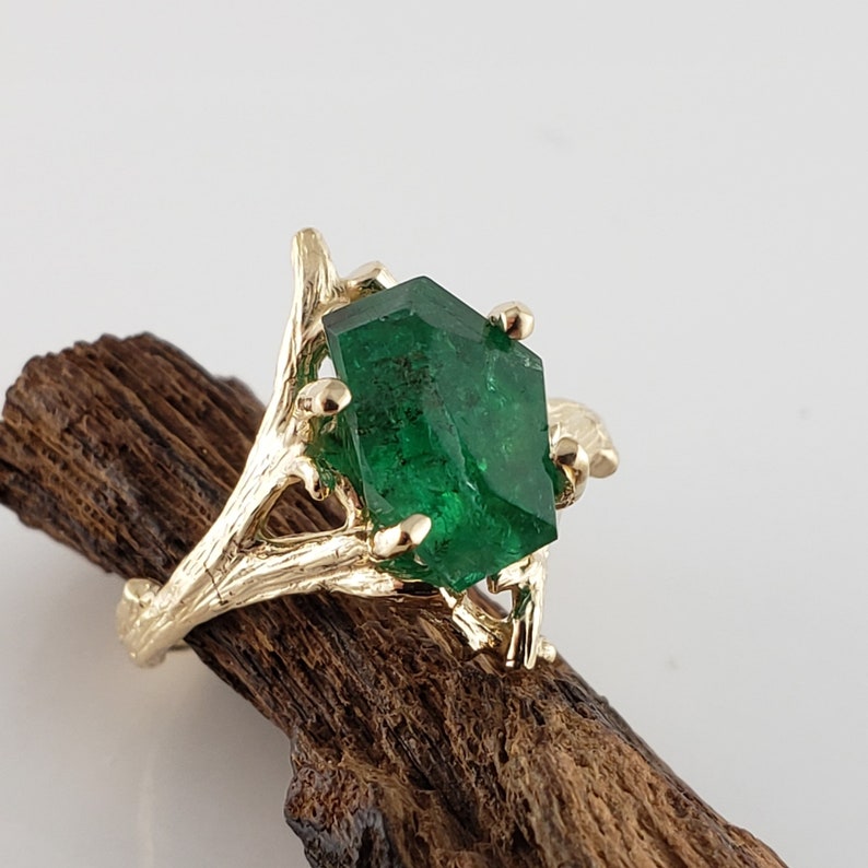 Puede incluir: Un anillo de oro con una gran esmeralda facetada engastada en un dise&ntilde;o de rama.