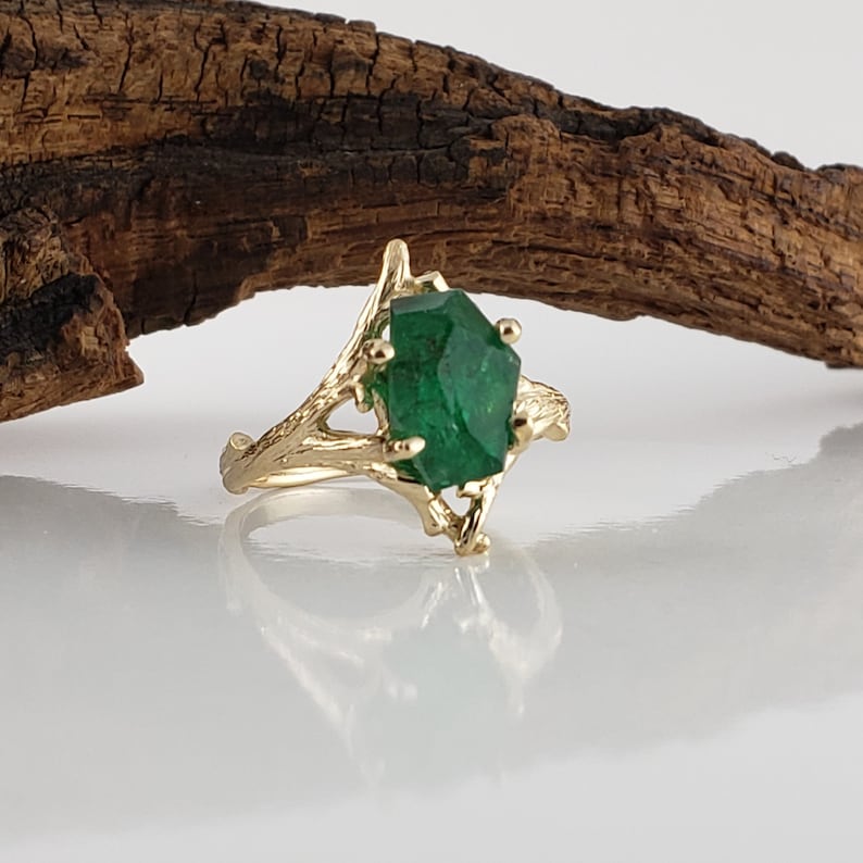 Puede incluir: Un anillo de oro con una piedra preciosa verde engastada en un dise&ntilde;o de rama.