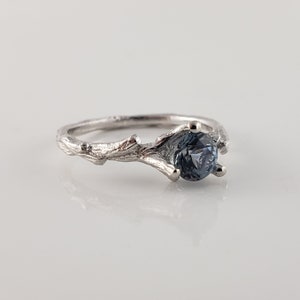 May include: A silver ring featuring a branch design with a blue gemstone set in the centre.