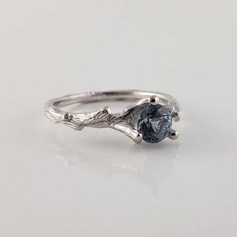 May include: A silver ring featuring a branch design with a blue gemstone set in the centre.