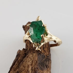 Puede incluir: Un anillo de oro con una gran esmeralda facetada engastada en un dise&ntilde;o de rama.