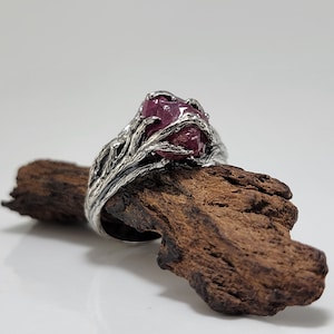 May include: A silver ring featuring a large, pink, rough-cut gemstone set in a tree branch design.