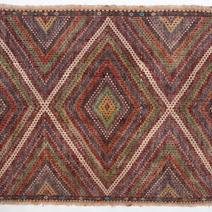May include: A rectangular woven rug with a geometric diamond pattern. The rug features a central diamond design in shades of red, green, and brown, with white and beige accents. The border has a beige background with small geometric shapes.
