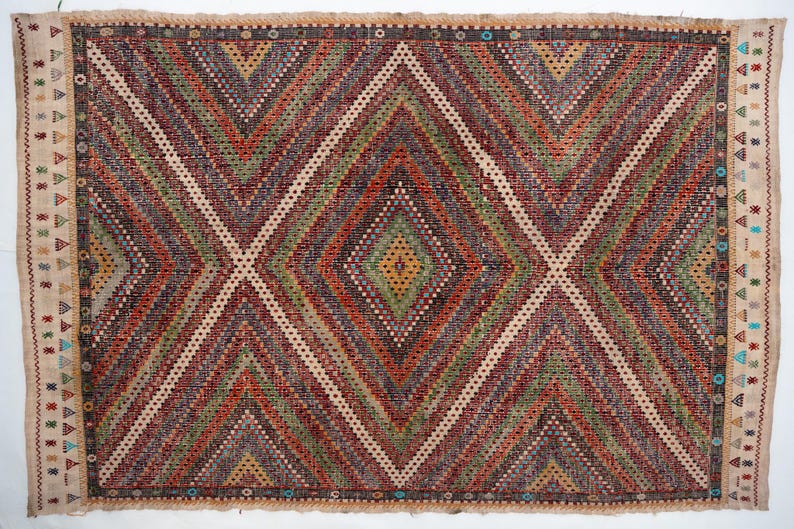 May include: A rectangular woven rug with a geometric diamond pattern. The rug features a central diamond design in shades of red, green, and brown, with white and beige accents. The border has a beige background with small geometric shapes.