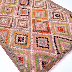 May include: A colorful, geometric rug with a diamond pattern. The rug features squares in shades of pink, orange, green, and black. The border has a repeating pattern of small squares. This rug is suitable for a living room or bedroom.