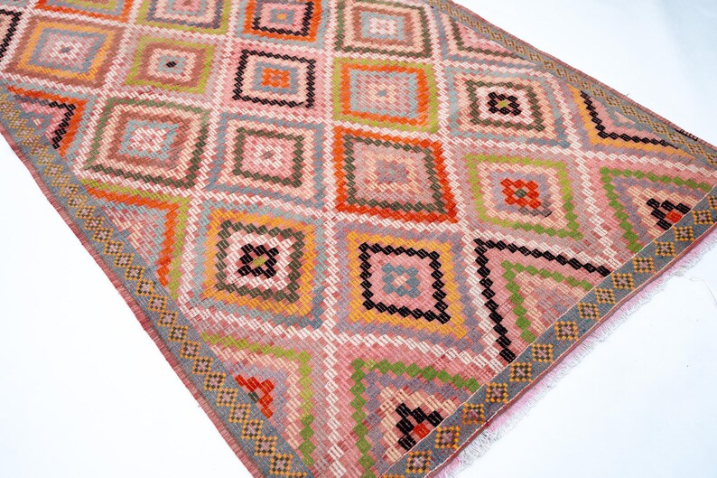 May include: A colorful, geometric rug with a diamond pattern. The rug features squares in shades of pink, orange, green, and black. The border has a repeating pattern of small squares. This rug is suitable for a living room or bedroom.
