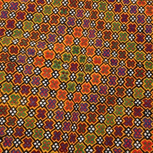 May include: Close-up of a colorful, patterned rug. The rug features a repeating floral design in shades of orange, red, purple, green, and white, set against a yellow background. The pattern is outlined in black, creating a geometric effect.