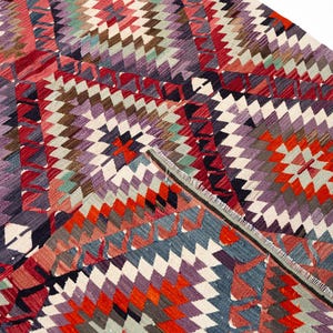 Puede incluir: Una alfombra colorida con un dise&ntilde;o geom&eacute;trico y un dise&ntilde;o de diamantes. La alfombra presenta una variedad de colores, incluyendo rojo, naranja, morado, blanco y azul. La alfombra est&aacute; hecha de tela tejida y tiene un borde con flecos.