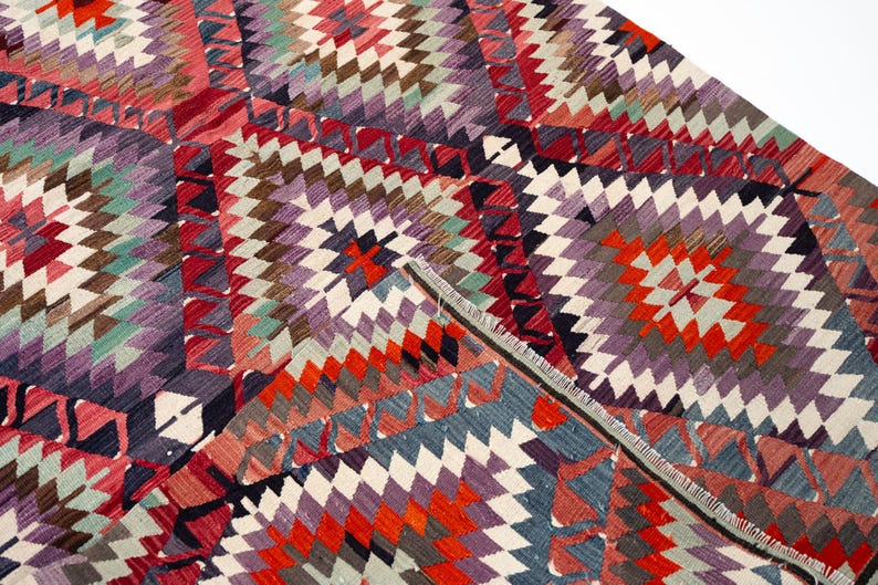 Puede incluir: Una alfombra colorida con un dise&ntilde;o geom&eacute;trico y un dise&ntilde;o de diamantes. La alfombra presenta una variedad de colores, incluyendo rojo, naranja, morado, blanco y azul. La alfombra est&aacute; hecha de tela tejida y tiene un borde con flecos.