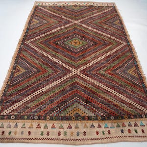 May include: Rectangular woven rug with a geometric diamond pattern in shades of red, green, brown, and cream. The rug has a cream-coloured border with small triangle and zigzag designs. The rug is approximately 152 cm long and 91 cm wide.