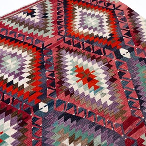 Puede incluir: Una vibrante alfombra con un dise&ntilde;o geom&eacute;trico de diamantes. La alfombra presenta una mezcla de colores, incluyendo rojo, morado, blanco y turquesa. El dise&ntilde;o es intrincado, con un patr&oacute;n repetido de diamantes y tri&aacute;ngulos.