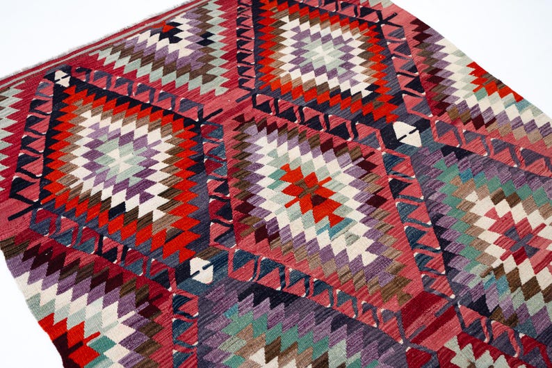 Puede incluir: Una vibrante alfombra con un dise&ntilde;o geom&eacute;trico de diamantes. La alfombra presenta una mezcla de colores, incluyendo rojo, morado, blanco y turquesa. El dise&ntilde;o es intrincado, con un patr&oacute;n repetido de diamantes y tri&aacute;ngulos.