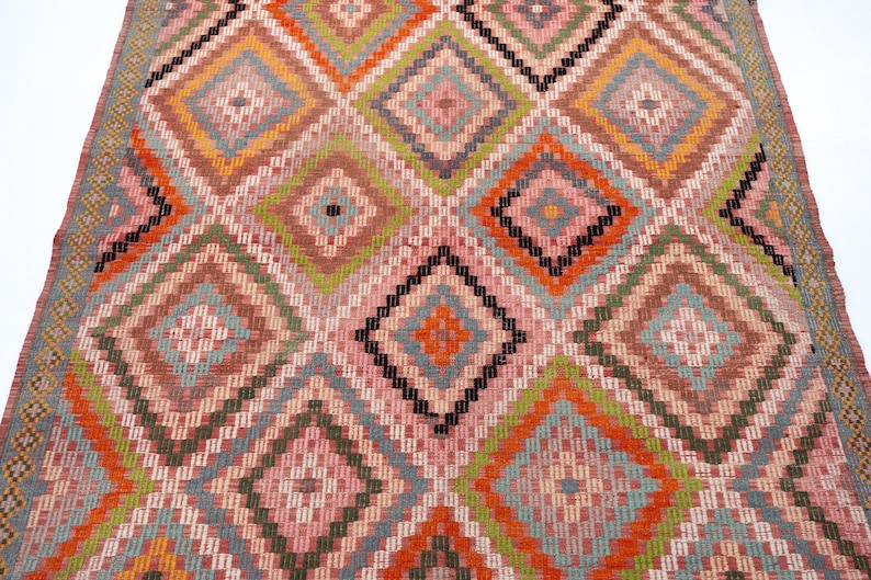 May include: A colorful rug with a geometric diamond pattern. The rug features a repeating design of diamonds in shades of pink, orange, green, and blue, with black accents. The rug is likely made of woven fabric.